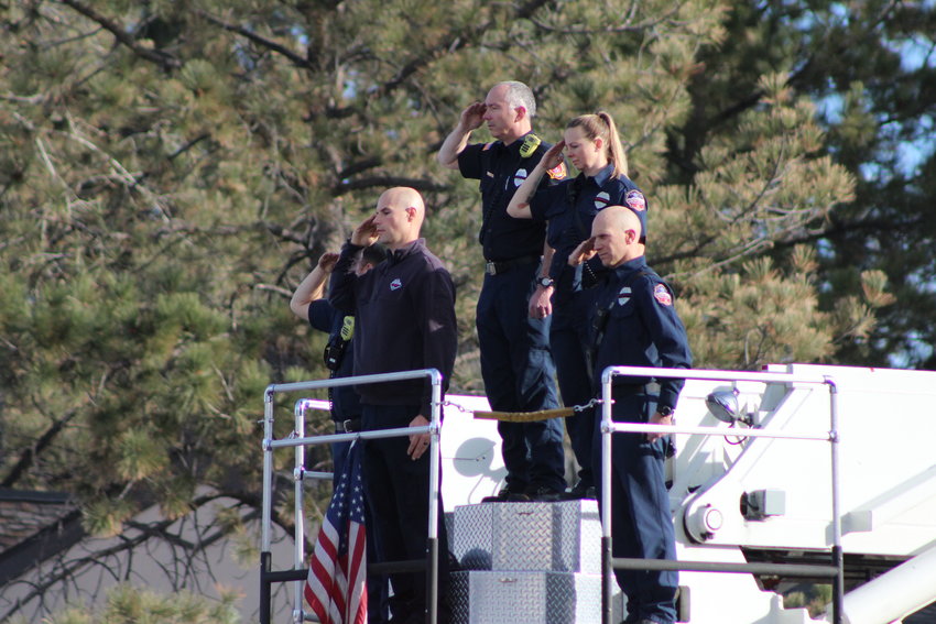 Fire fighters from the Castle Rock Fire Department stand atop a firetruck and salute as the procession for Troy Jackson drives through Centennial Dec. 20.